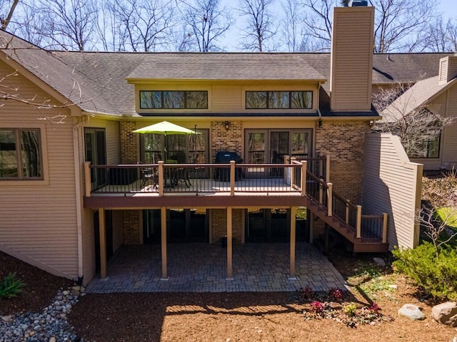 rear view of house with brick siding, a patio area, roof with shingles, and a deck
