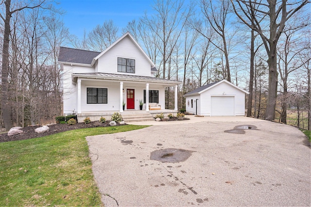 view of front of house featuring a standing seam roof, a detached garage, covered porch, an outdoor structure, and aphalt driveway