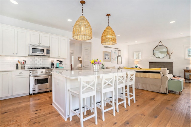 kitchen featuring white cabinets, stainless steel appliances, open floor plan, a kitchen bar, and light countertops