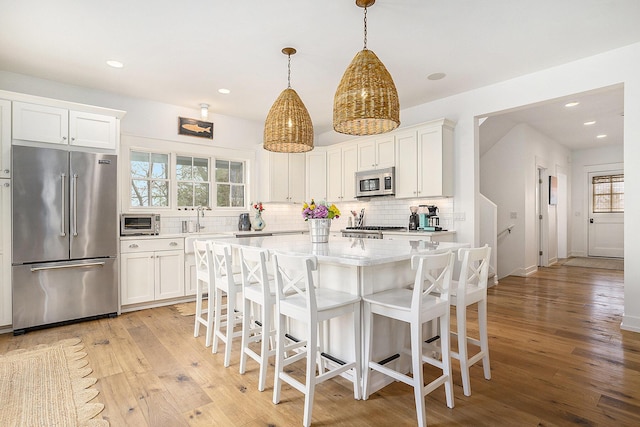 kitchen with backsplash, light wood finished floors, appliances with stainless steel finishes, and white cabinetry