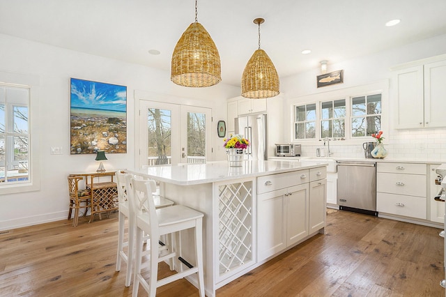 kitchen with white cabinets, stainless steel appliances, a sink, light wood-style floors, and decorative backsplash