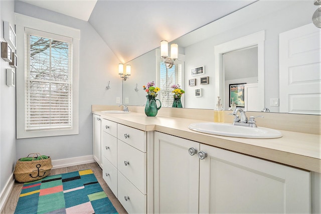 bathroom with vaulted ceiling, a sink, double vanity, and baseboards