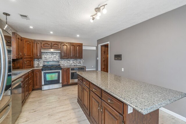 11886 Riverside Dr, White Pigeon, MI 49099 - kitchen featuring a textured ceiling, decorative backsplash, under cabinet range hood, a kitchen island, and appliances with stainless steel finishes