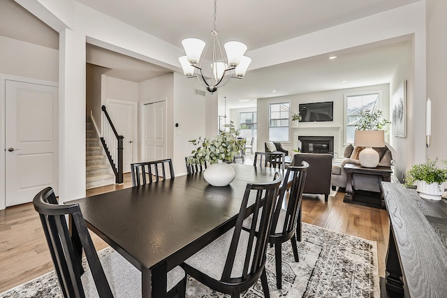 dining room featuring recessed lighting, light wood finished floors, a chandelier, a glass covered fireplace, and stairs