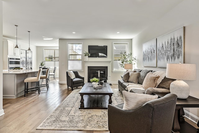 living room with recessed lighting, a glass covered fireplace, light wood-style flooring, and baseboards