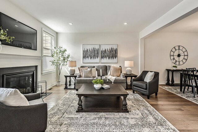 living area featuring a glass covered fireplace, baseboards, wood finished floors, and recessed lighting