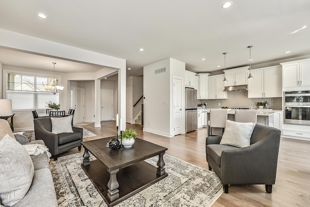 living room featuring light wood-style floors, stairway, visible vents, and an inviting chandelier