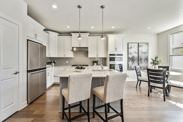 kitchen featuring under cabinet range hood, stainless steel appliances, light countertops, a sink, and decorative backsplash