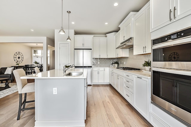 kitchen with under cabinet range hood, stainless steel appliances, backsplash, a sink, and a breakfast bar area
