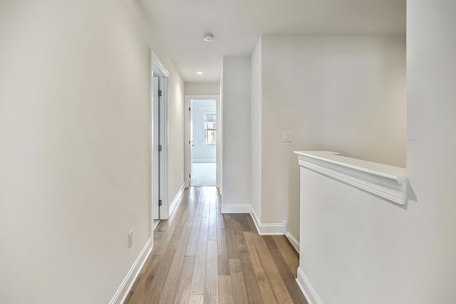 hall featuring baseboards, hardwood / wood-style floors, and recessed lighting