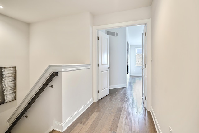 corridor with hardwood / wood-style floors, visible vents, baseboards, and an upstairs landing