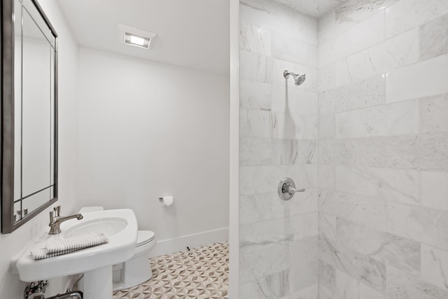 bathroom featuring a tile shower, toilet, a sink, and baseboards