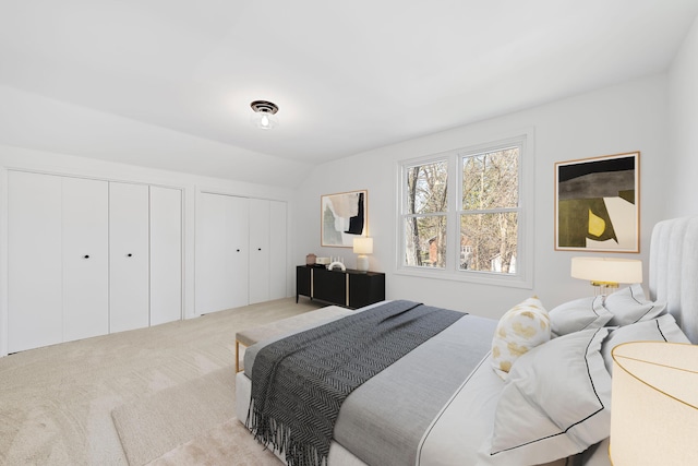 carpeted bedroom with vaulted ceiling, visible vents, and two closets