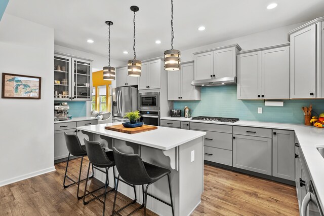 5849 Gavin Ln, Kalamazoo, MI 49009 - kitchen with under cabinet range hood, gray cabinetry, appliances with stainless steel finishes, and a kitchen bar