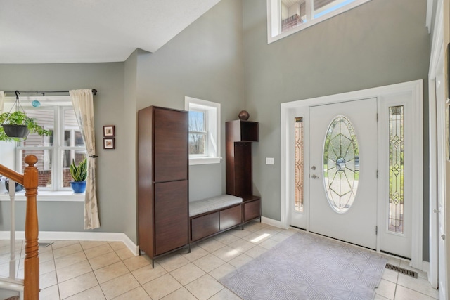 entrance foyer with light tile patterned flooring, a towering ceiling, visible vents, and plenty of natural light