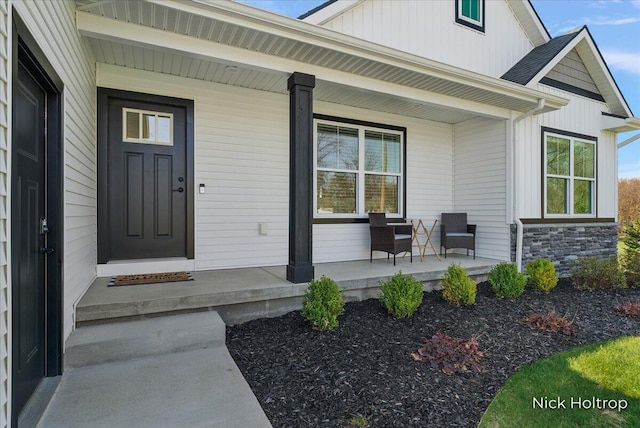 doorway to property with board and batten siding, a porch, and stone siding