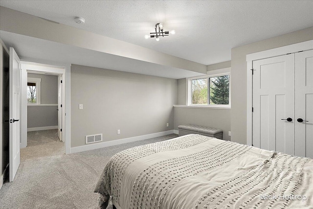 bedroom with a textured ceiling, baseboards, visible vents, carpet, and a closet