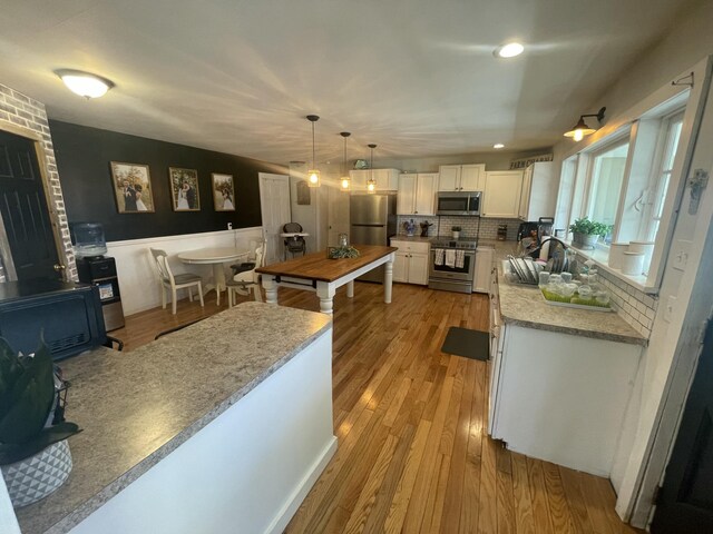kitchen featuring white cabinets, a sink, light wood-style floors, decorative backsplash, and appliances with stainless steel finishes