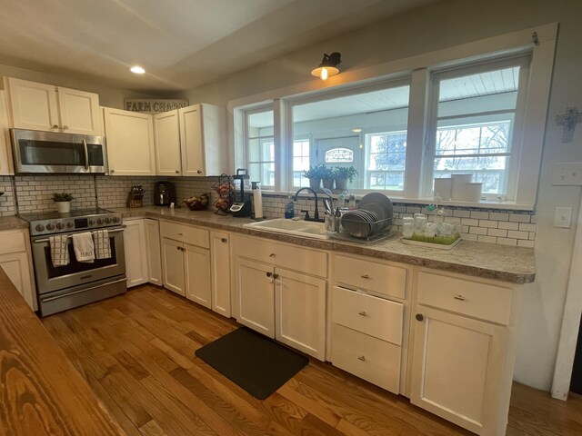 kitchen featuring a sink, decorative backsplash, stainless steel appliances, dark wood finished floors, and white cabinetry
