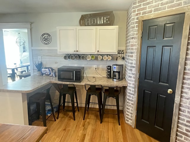 kitchen featuring white cabinets, light wood finished floors, light countertops, a breakfast bar, and black microwave