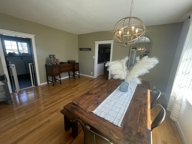 dining room with independent washer and dryer, wood finished floors, baseboards, and an inviting chandelier