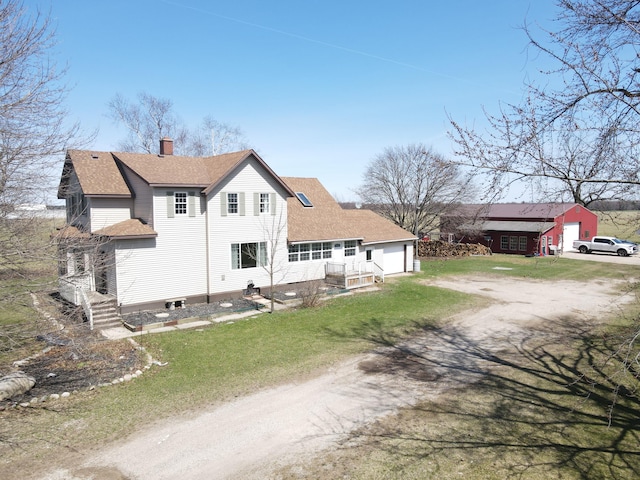 back of property featuring dirt driveway, a chimney, roof with shingles, and an outbuilding