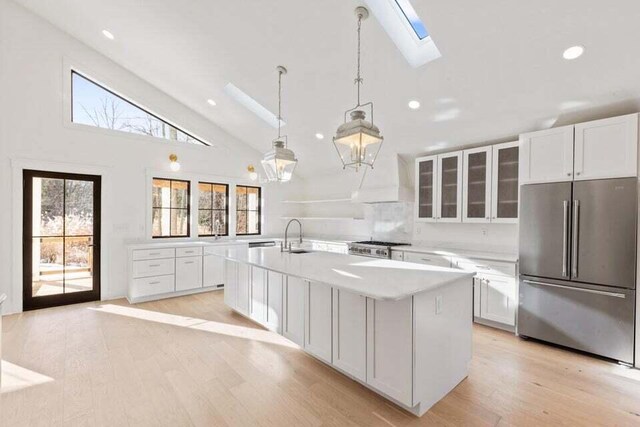 kitchen featuring white cabinetry, a skylight, glass insert cabinets, high end fridge, and light countertops
