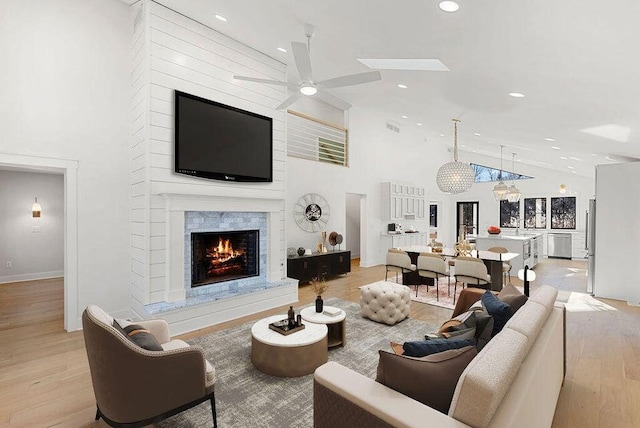 living room featuring high vaulted ceiling, a fireplace, a ceiling fan, and light wood-style flooring