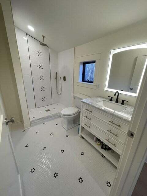 bathroom with a tile shower, toilet, and vanity