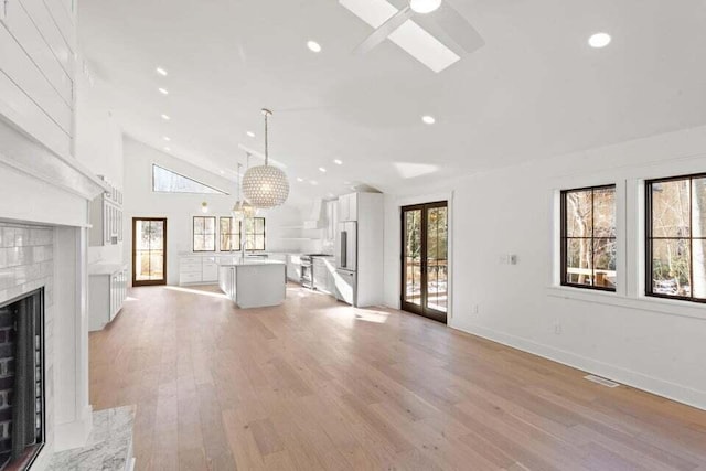 unfurnished living room featuring a fireplace with flush hearth, a sink, visible vents, light wood-style floors, and ceiling fan with notable chandelier