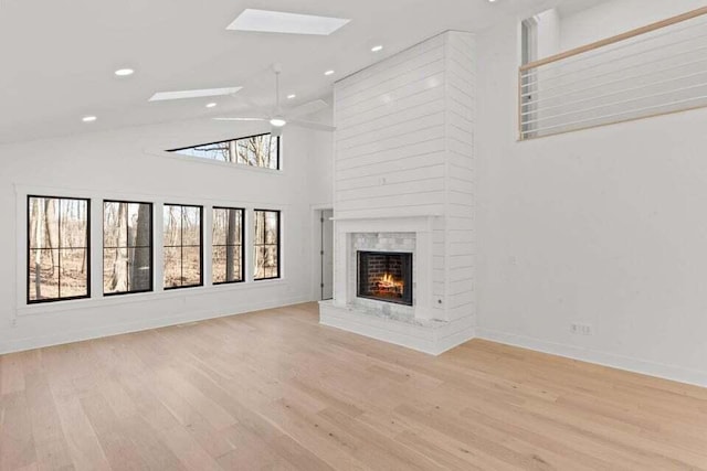 unfurnished living room featuring recessed lighting, wood finished floors, a skylight, a fireplace, and ceiling fan