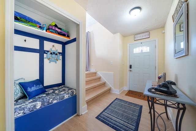 foyer entrance with baseboards, wood finished floors, a textured ceiling, and stairs