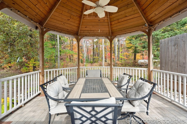 wooden terrace featuring outdoor dining area, a ceiling fan, and a gazebo