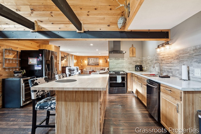 kitchen with light brown cabinets, wall chimney range hood, a sink, appliances with stainless steel finishes, and beam ceiling