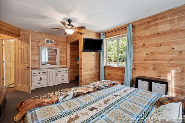 bedroom featuring dark carpet, ceiling fan, wood walls, and visible vents