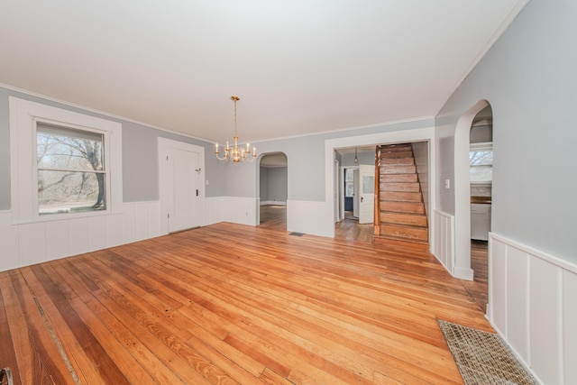 unfurnished dining area with arched walkways, light wood-type flooring, a wainscoted wall, and ornamental molding