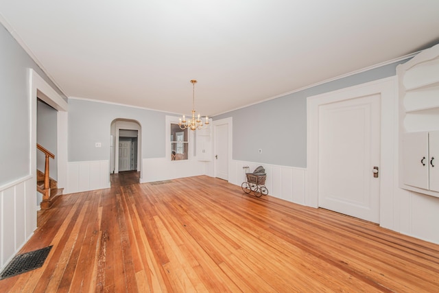 unfurnished dining area with hardwood / wood-style floors, arched walkways, an inviting chandelier, a wainscoted wall, and visible vents