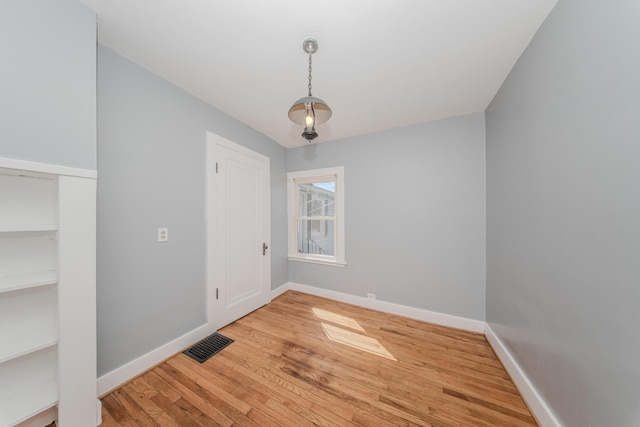 spare room featuring wood finished floors, visible vents, and baseboards