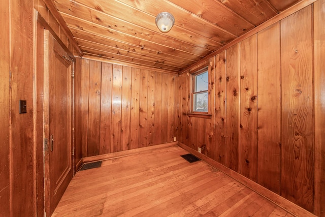 empty room featuring wooden ceiling, wood walls, visible vents, and light wood-type flooring