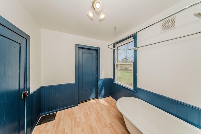 interior space with wainscoting, a freestanding tub, wood finished floors, and visible vents