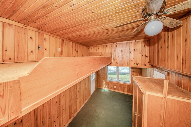 interior space featuring carpet flooring, wooden walls, wooden ceiling, and a ceiling fan