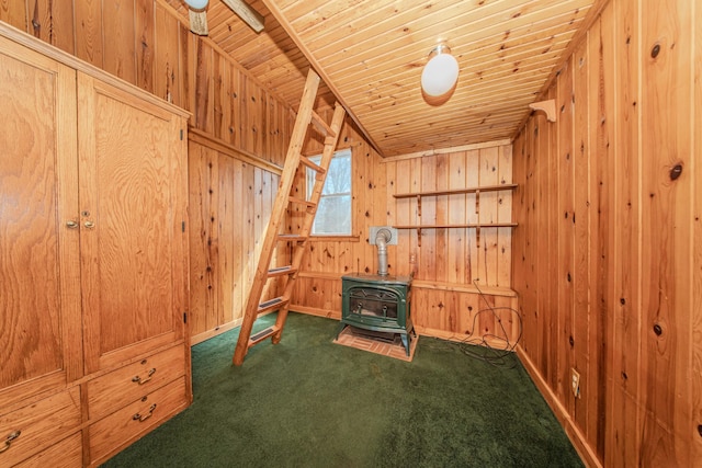 interior space featuring dark colored carpet, wooden ceiling, baseboards, wooden walls, and a wood stove