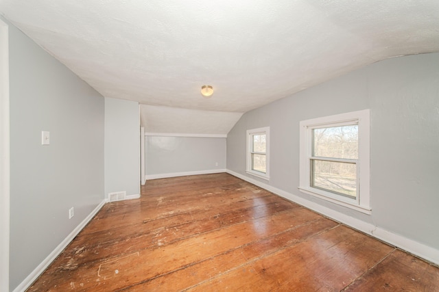 bonus room featuring hardwood / wood-style flooring, vaulted ceiling, visible vents, and baseboards