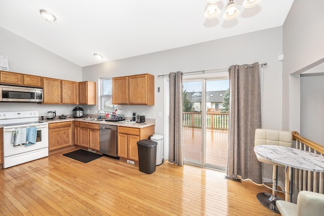 kitchen featuring an inviting chandelier, vaulted ceiling, a sink, light wood-style floors, and appliances with stainless steel finishes