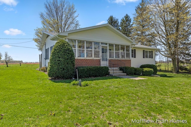 view of front of house with brick siding, a front lawn, and a sunroom