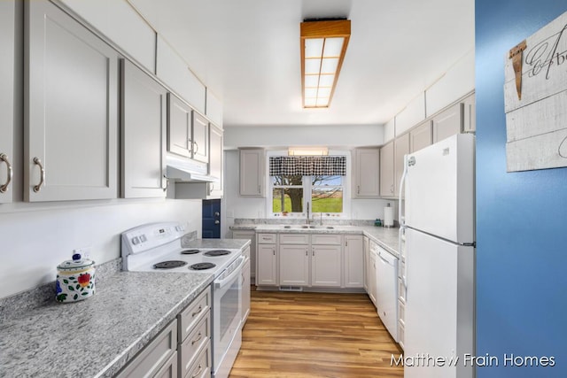 kitchen with under cabinet range hood, a sink, white appliances, light wood-type flooring, and light stone countertops