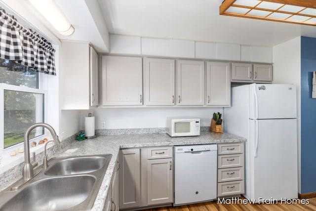 kitchen with gray cabinets, wood finished floors, a sink, and white appliances