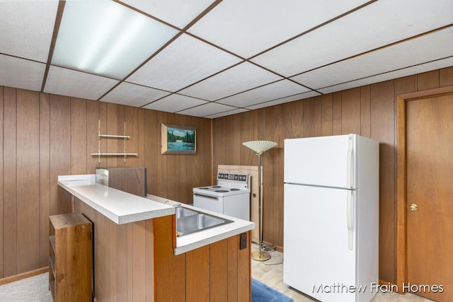kitchen featuring brown cabinets, wooden walls, white appliances, and a paneled ceiling