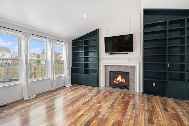unfurnished living room with lofted ceiling, wood finished floors, baseboards, a tiled fireplace, and built in features