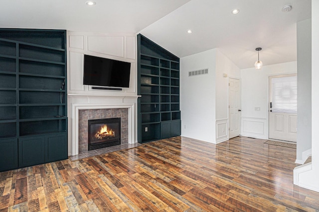 unfurnished living room with visible vents, wood finished floors, built in features, and vaulted ceiling